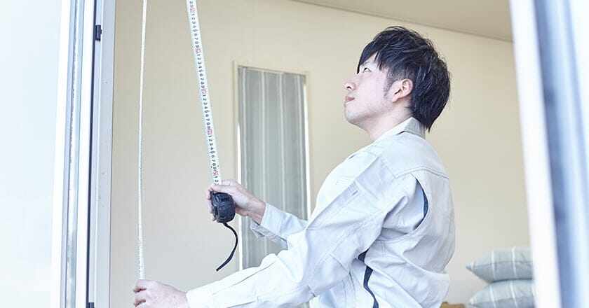 カーテンのサイズを測っている男性の写真